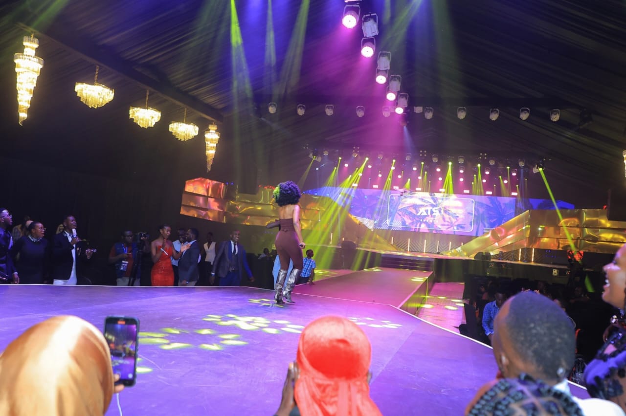 Performer on a lit runway stage during a live show with audience watching